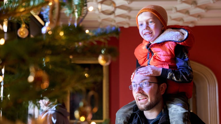 Family enjoying the Christmas decorations in the Victorian manor house at Hughenden. Child on the man's shoulders.